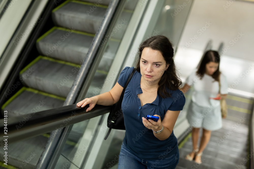Woman with phone moving up on escalator