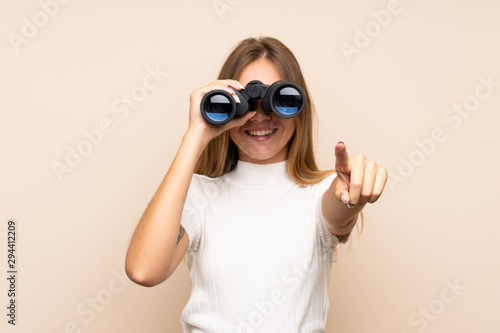 Young blonde woman over isolated background with black binoculars photo