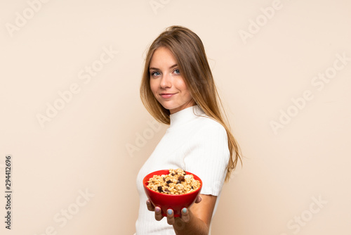 Young blonde woman over isolated background holding a bowl of cereals