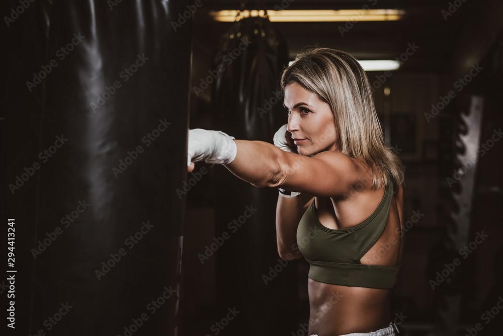 Muscular pretty woman is doing her kickboxing exercises with punching bag.