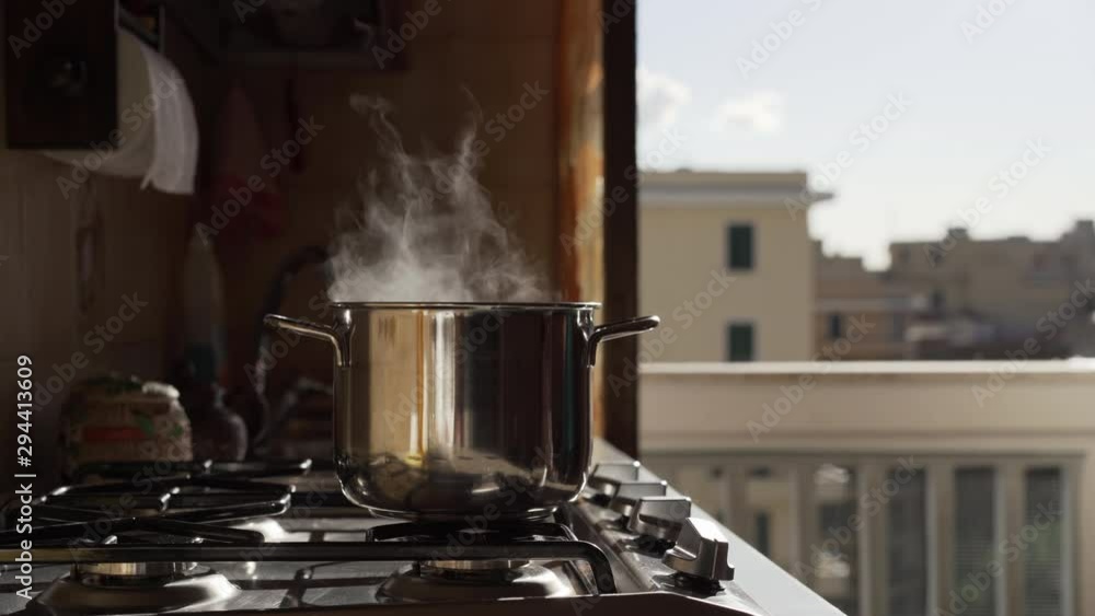Boiling cooking pan on heating stove on balcony background. Gas flame heating pot and white steam rising from it on the background of solar glare. Physical effects and abstract processes concept Boiling cooking pan on heating stove on balcony background. Gas flame heating pot and white steam rising from it on the background of solar glare. Physical effects and abstract processes concept