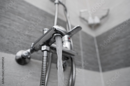 Water flows from the mixer. Modern designer tap and shower in bathroom. Closeup of chrome shower, faucet, in the bathroom covered decorative ceramic. Mixer cold hot water.