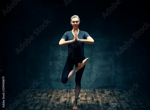 Fototapeta Naklejka Na Ścianę i Meble -  Young beautiful woman doing yoga asana half bound lotus tree pose in dark room