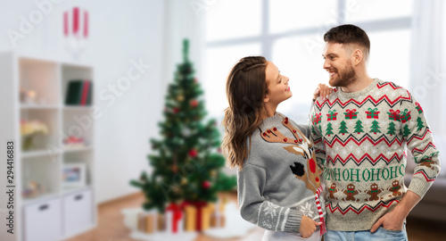 christmas, people and holidays concept - portrait of happy couple at ugly sweater party over home room background