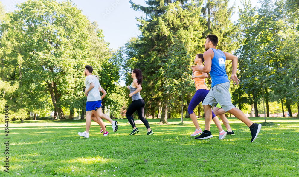 fitness, sport, race and healthy lifestyle concept - group of happy people or sportsmen running marathon with badge numbers at summer park fitness, sport, race and healthy lifestyle concept - group of happy people or sportsmen running marathon with badge numbers at summer park