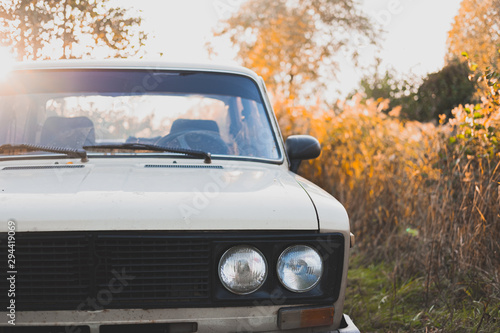 Old soviet car in sunset, detailed front view. Retro aesthetics concept, old vehicle among beautiful autumn plants