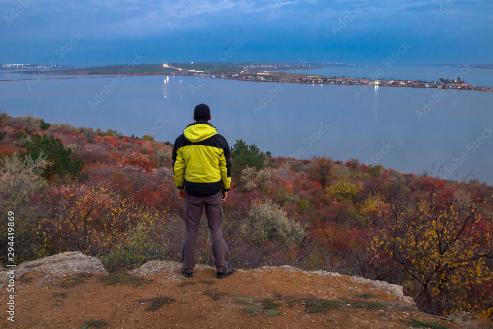 man hiker standing on the edge and admire of vanilla sunrise on the lake, lights of road