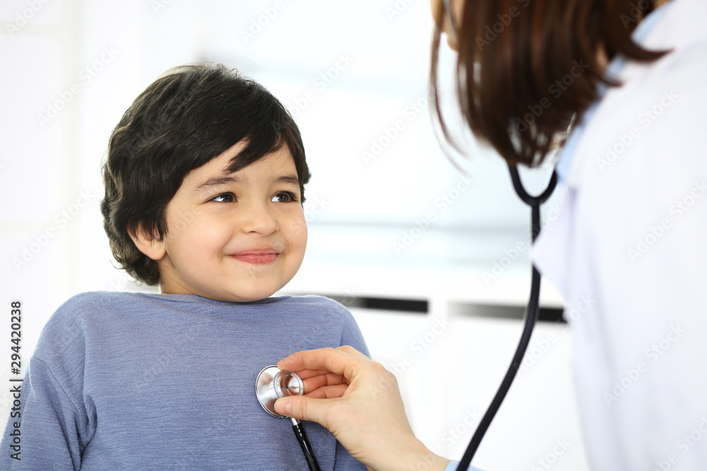 Doctor examining a child patient by stethoscope. Cute arab boy at physician appointment. Medicine and healthcare concept Doctor examining a child patient by stethoscope. Cute arab boy at physician appointment. Medicine and healthcare concept