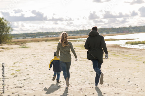 family, leisure and people concept - happy mother, father and little son running along autumn beach
