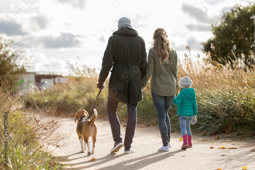 family, pets and people concept - happy mother, father and little daughter walking with beagle dog in autumn