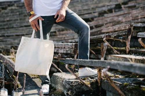 Young man holding white textile eco bag against urban city background. Ecology or environment protection concept. White eco bag for mock up.