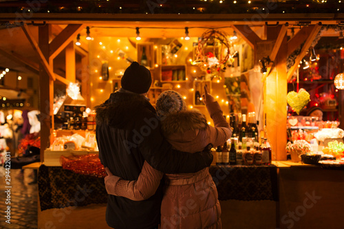 love, winter holidays and people concept - happy senior couple hugging at christmas market souvenir shop stall in evening photo