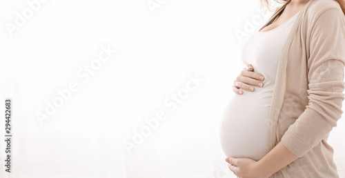 Pregnant woman embracing her belly, white panorama background