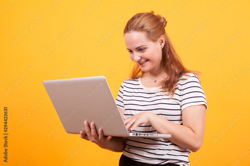 Girl smiling browsing on laptop in studio over yellow background Girl smiling browsing on laptop in studio over yellow background