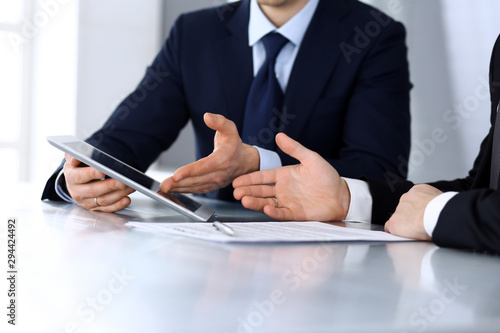 Business people using tablet computer while working together at the desk in modern office. Unknown businessman or male entrepreneur with colleague at workplace. Teamwork and partnership concept