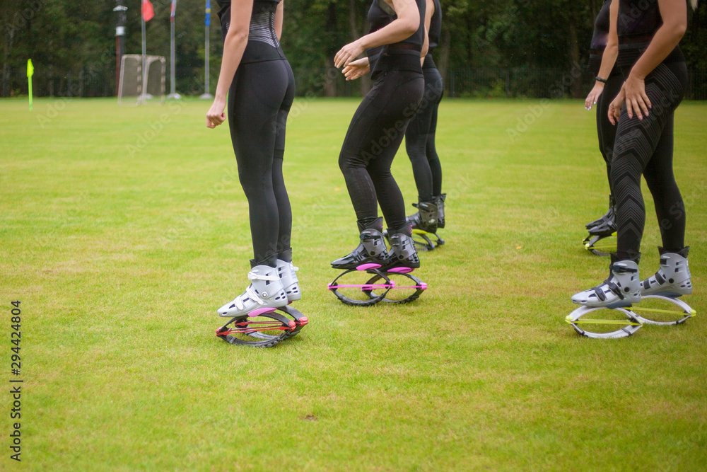 Obraz premium Girls in boots for jumping. Bouncing shoes on the legs of women. Sports performance on the football field in the rain. A new sport is jumping in special shoes on springs.