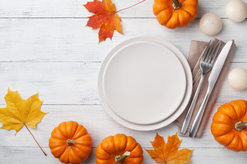 Autumn Thanksgiving table setting for dinner with plate, knife, fork decorated pumpkins and maple leaves. Top view.