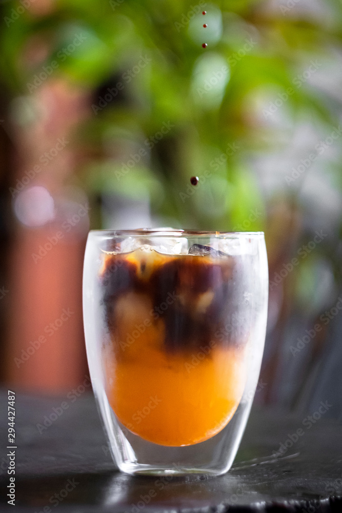 Iced fresh orange juice topped with espresso on wooden table in a garden; as sunrise coffee make a good day. Iced fresh orange juice topped with espresso on wooden table in a garden; as sunrise coffee make a good day.