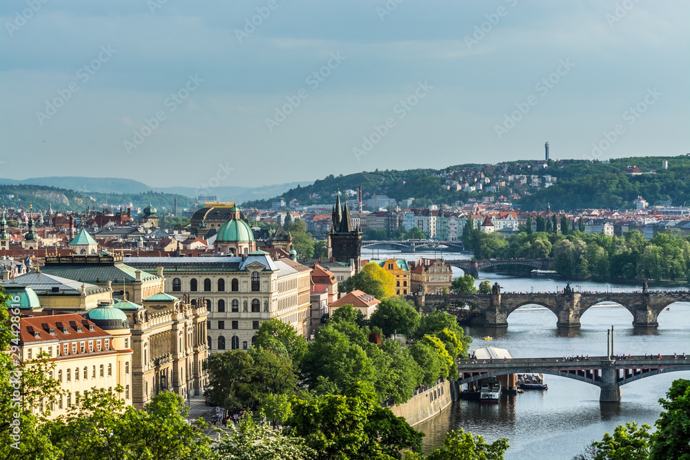 Fototapeta premium Aerial view of citycape of old town of Prague, with a lot of rooftops, churches, and the landmark of Charles Bridge, and Vltava river.
