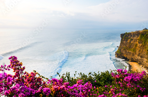 Seascape, ocean at sunset. Flowers on ocean landscape background near Uluwatu temple at sunset, Bali, Indonesia. Bougainvillea flowers at the foreground.