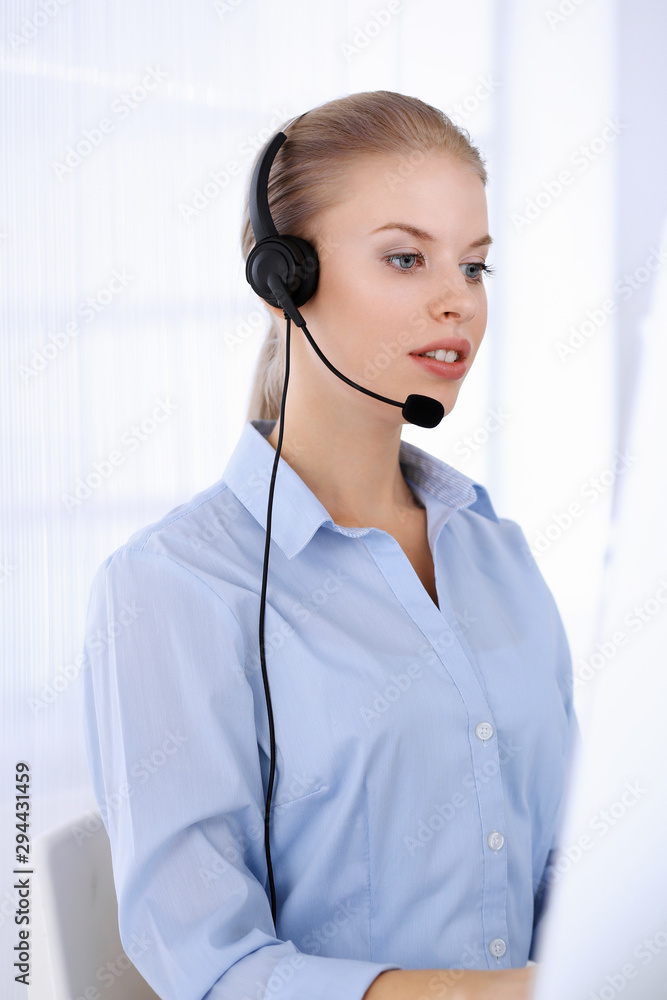 Call center office. Beautiful blonde woman using computer and headset for consulting clients online. Group of operators working as customer service occupation. Business people concept Call center office. Beautiful blonde woman using computer and headset for consulting clients online. Group of operators working as customer service occupation. Business people concept