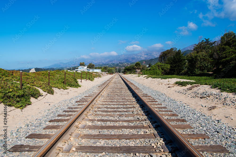 Fototapeta premium Railroad tracks converging in perpective into the distance towards distant mountains