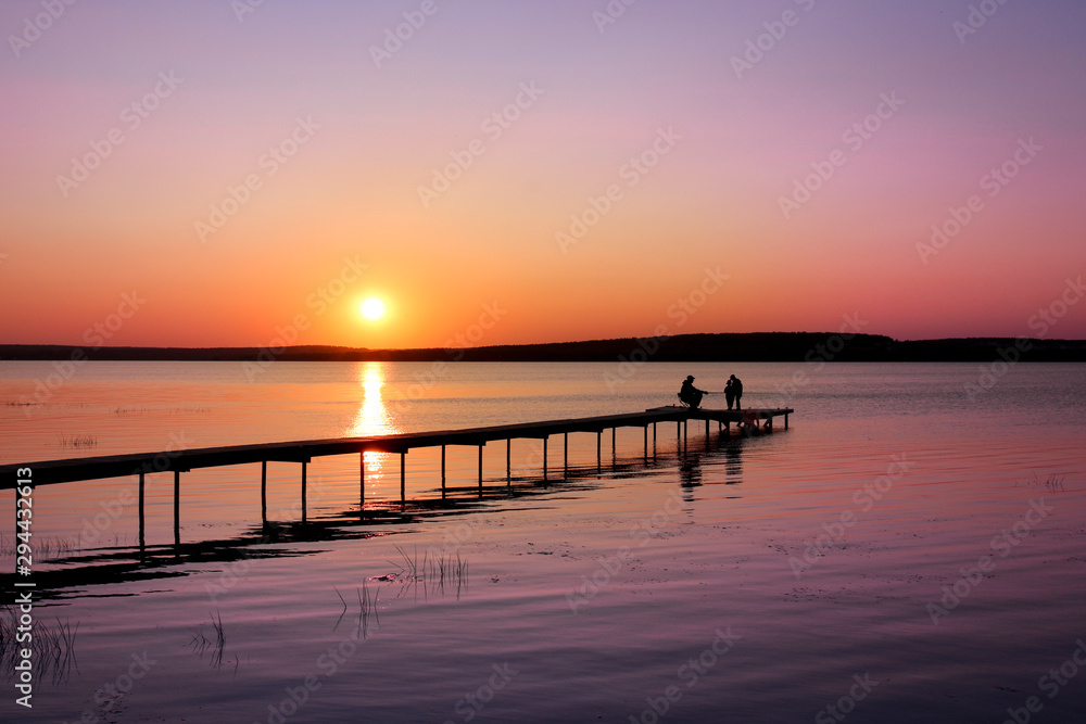 Colorful sunset over the lake with a pier. A fisherman is fishing on the pier and the children came to see. Pink and purple pastel watercolor soft tones.