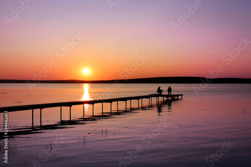 Colorful sunset over the lake with a pier. A fisherman is fishing on the pier and the children came to see. Pink and purple pastel watercolor soft tones.