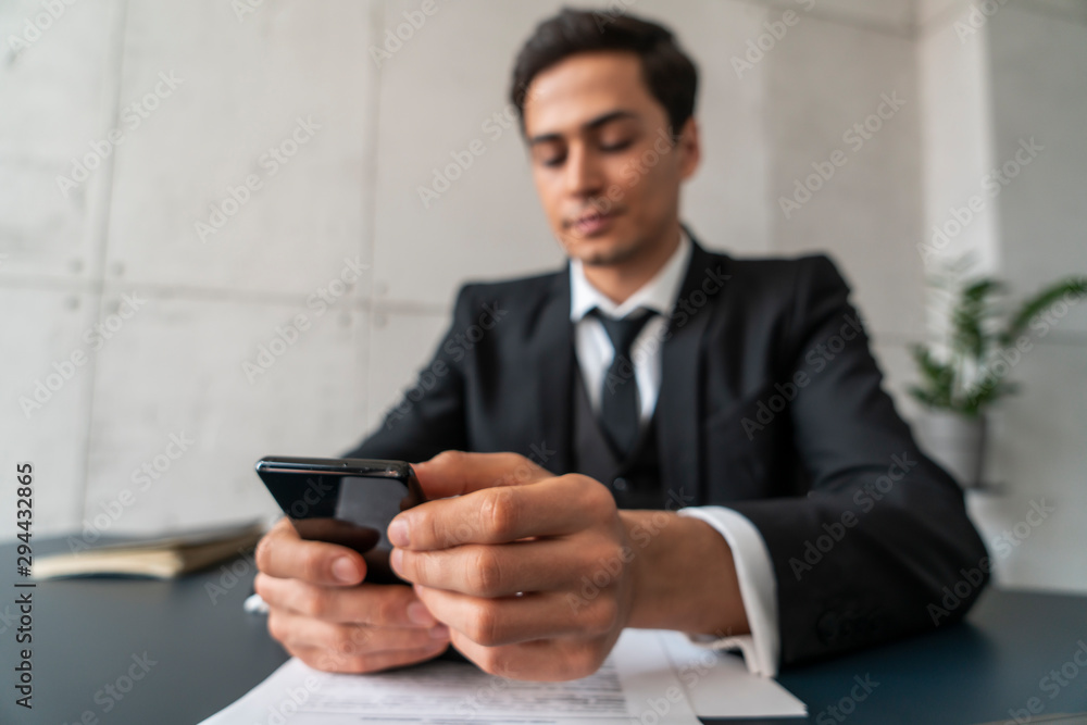 Blurred young businessman using smartphone at loft office table with contract and copybook. Concept of internet and communication Blurred young businessman using smartphone at loft office table with contract and copybook. Concept of internet and communication