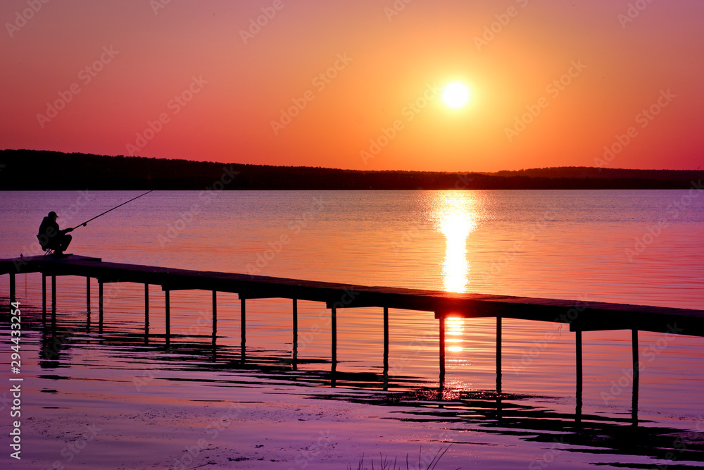 Colorful sunset over the lake with a pier. A lone fisherman is fishing on the pier. Pink and purple pastel watercolor soft tones.