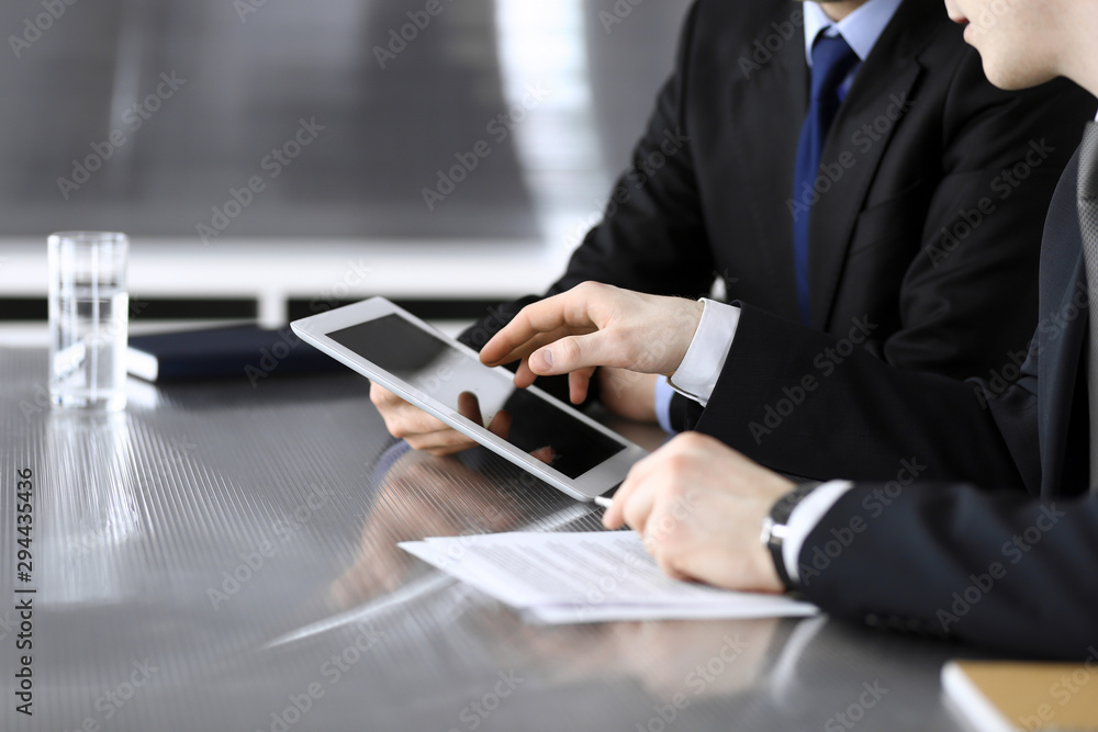 Businessman using tablet computer and work together with his colleague or partner at the glass desk in modern office, close-up. Unknown business people at meeting. Teamwork and partnership concept Businessman using tablet computer and work together with his colleague or partner at the glass desk in modern office, close-up. Unknown business people at meeting. Teamwork and partnership concept