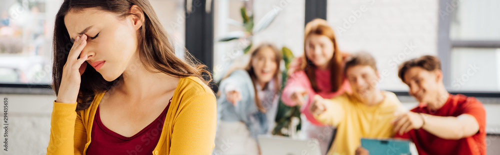 panoramic shot of sad girl and laughing schoolchildren pointing with fingers at her panoramic shot of sad girl and laughing schoolchildren pointing with fingers at her