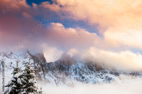 Mountain peaks with clouds at sunset. Snow-covered winter Dolomite Alps. Val Di Fassa, Italy. Beautiful winter landscape