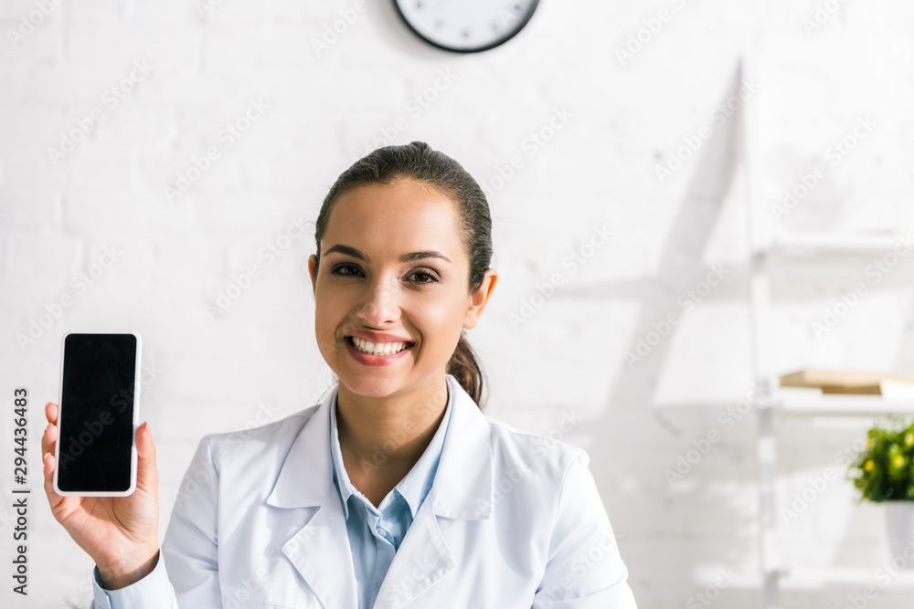 happy doctor in white coat looking at camera and holding smartphone with blank screen happy doctor in white coat looking at camera and holding smartphone with blank screen