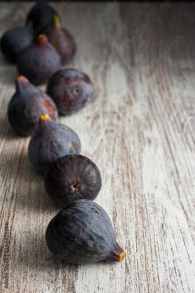 Fototapeta premium Top view on purple figs with bokeh effect in the background on light wood in vertical