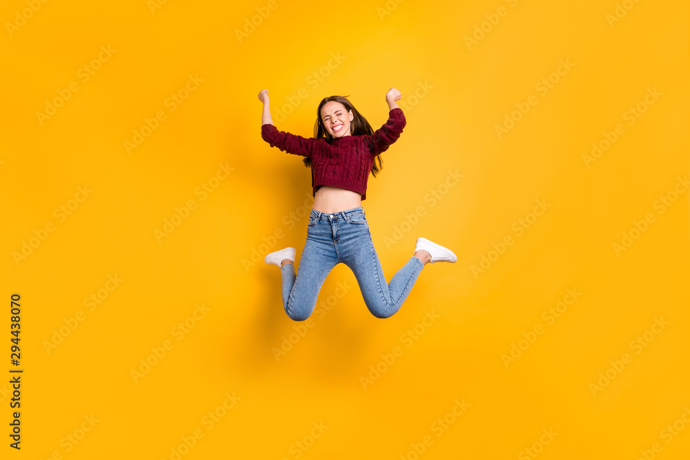 Full length photo of delighted woman with her closed eyes and long haircut raising fists wearing burgundy sweater isolated over yellow background