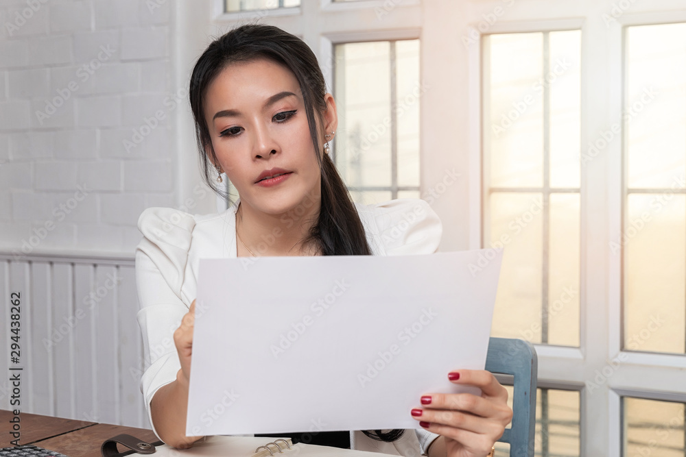 Young asian woman in smart casual wear holding document while sitting near window in retro home office. Young asian woman in smart casual wear holding document while sitting near window in retro home office.