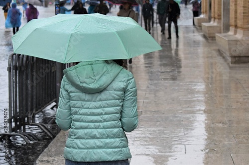 A woman with green jacket and green umbrella walks in the rain
