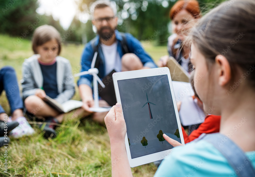 Fototapeta premium Group of school children with teacher and windmill model on field trip in nature.