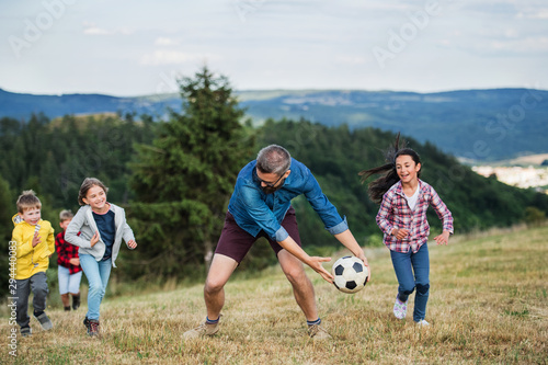 Group of school children with teacher on field trip in nature, playing with a ball.