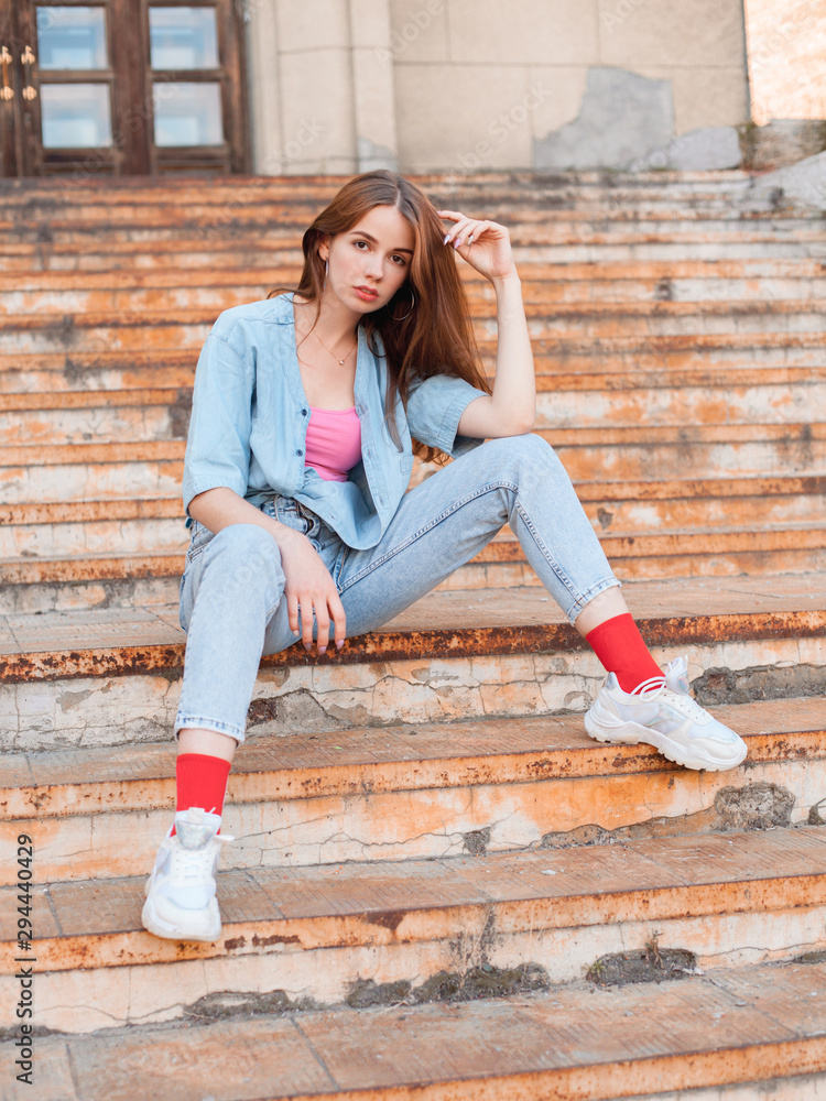Attractive young woman with brown hair sits on the stairs in the city
