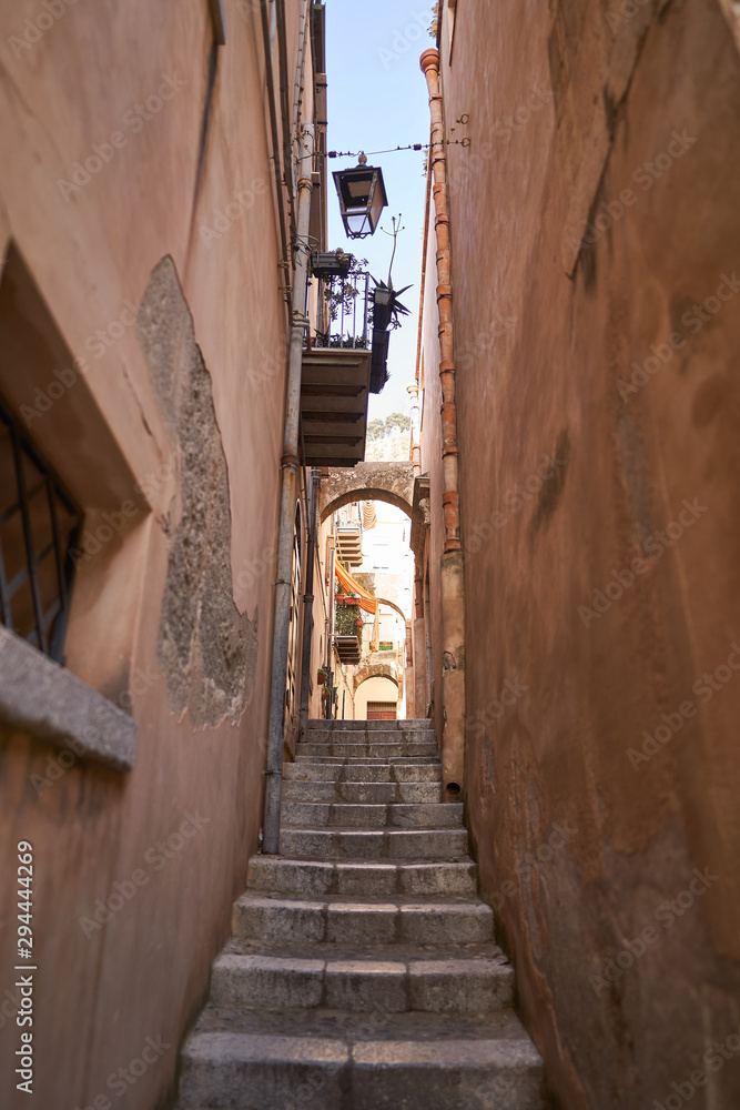 Thin or narrow small street in sicilian city Cefalu with  marble stone stairs hanging lantern and balcony. Typical example of historic and traditional mediterranean architecture taken in hot sunny day