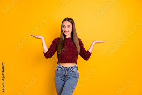 Portrait of lovely girl looking at her palms smiling wearing maroon pullover isolated over yellow background © deagreez