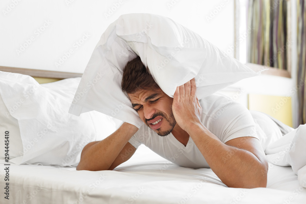 Sad man in bed covering head with pillow Sad man in bed covering head with pillow