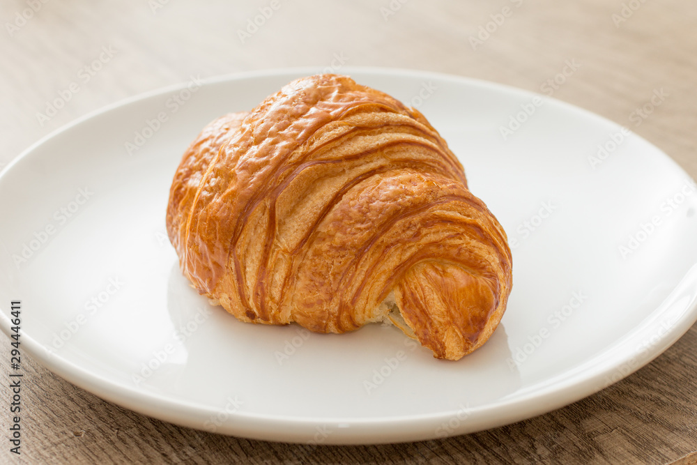 Food plate with croissant Dish showing bun of pastry. On rustic wooden table.