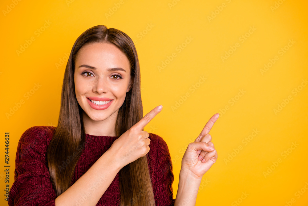 Close up photo of charming lady with long hairstyle pointing at copy space wearing maroon jumper isolated over yellow background Close up photo of charming lady with long hairstyle pointing at copy space wearing maroon jumper isolated over yellow background