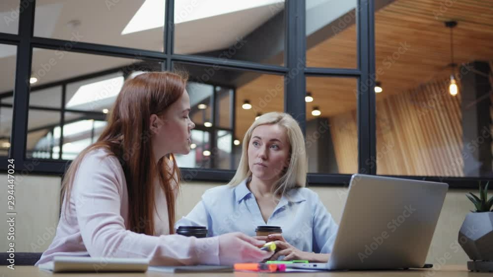 Young women in casual outfits analyzing data on laptop while sitting at table and working on project together Young women in casual outfits analyzing data on laptop while sitting at table and working on project together