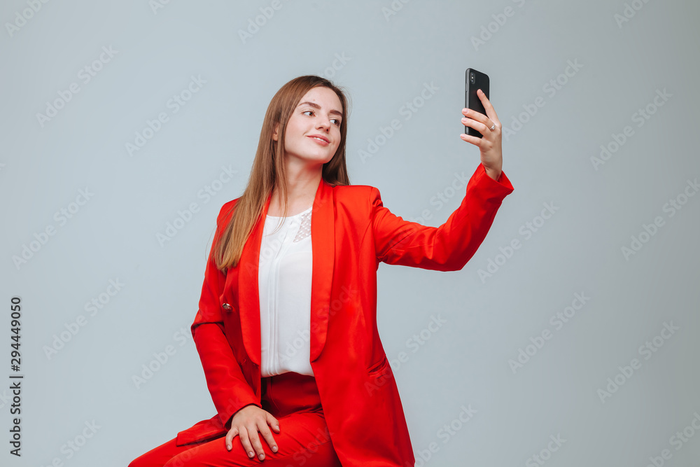 Naklejka premium girl in a red jacket takes a selfie on the phone on a gray background
