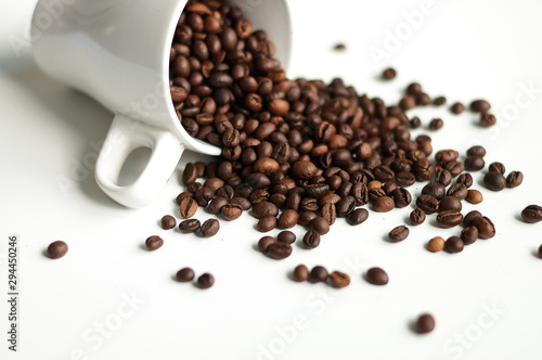 Roasted coffee sprinkled from a white bowl on a white background
