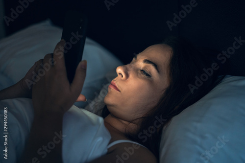 Young woman or girl using smartphone app social media while lying in bed at night